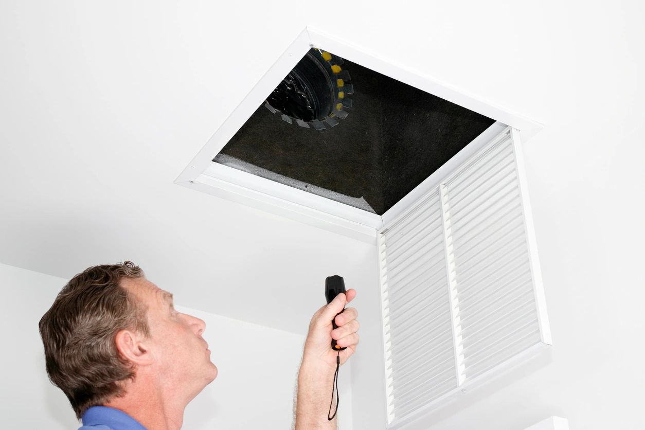 A man is looking up at the ceiling of an air vent.
